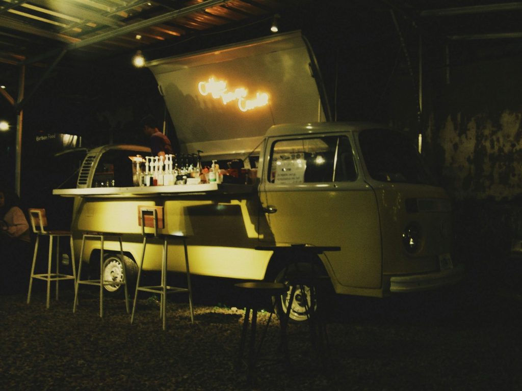 A classic yellow van converted into a food truck with neon lighting serving at night.